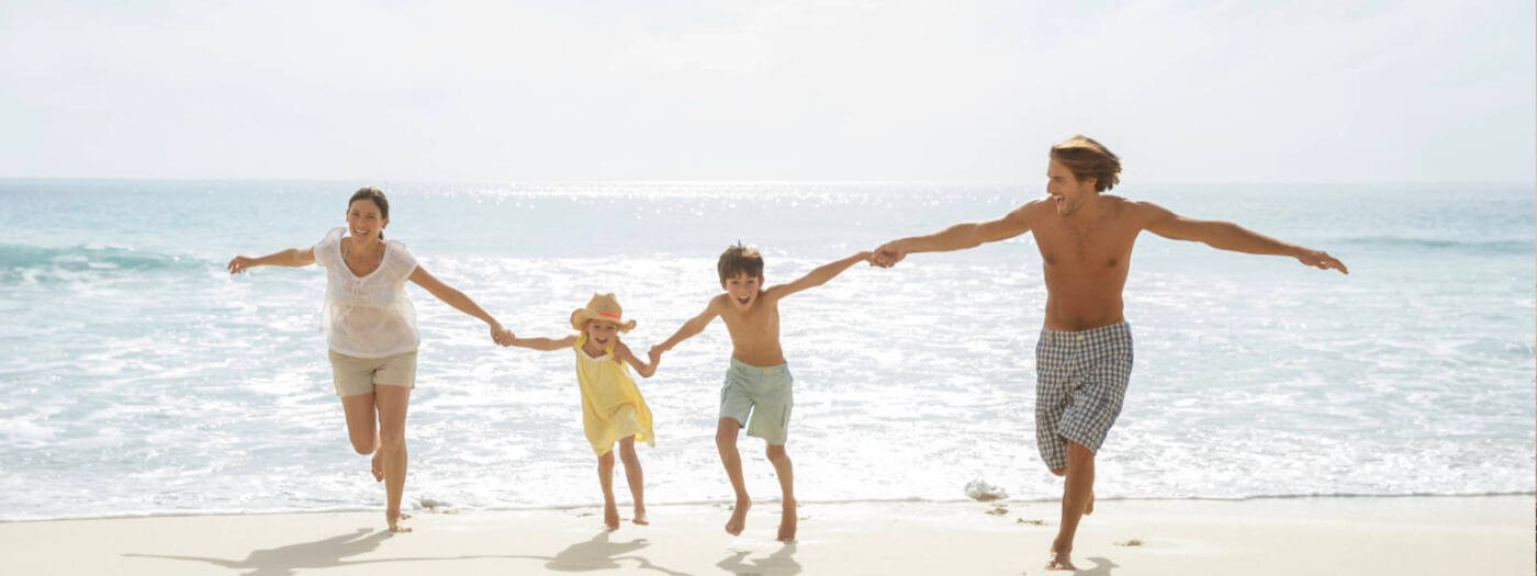 Happy family holding hands and running along a sunny beach, enjoying quality time by the ocean.